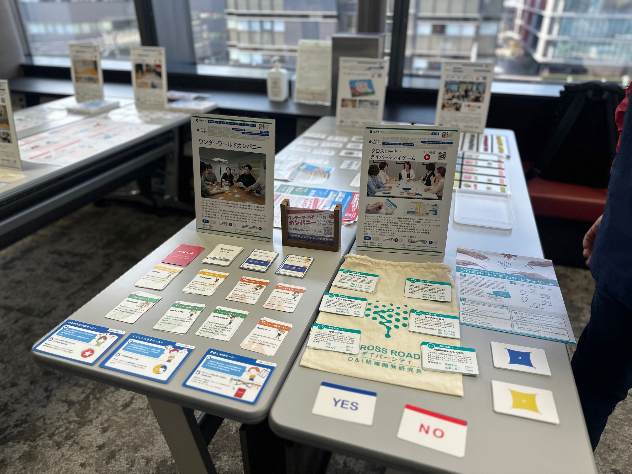 京都SDGsゲームショウに出展された、DEIコンサルティングに活用する「クロスロード・ダイバーシティゲーム」の展示ブースです。机上にはダイバーシティ研修で用いる多様な設問カードや解説パンフレットが並べられ、来場者へ専門的な学びの機会を提供しています。